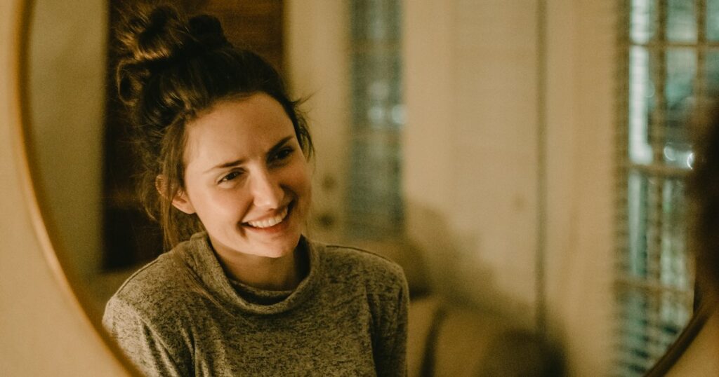 Mujer sonriendo frente a un espejo redondo mientras observa su sonrisa