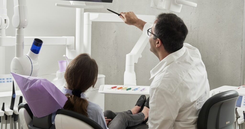 Dentista señala una pantalla mientras una paciente sentada en el sillón dental escucha la explicación