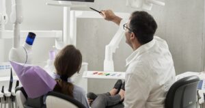Dentista señala una pantalla mientras una paciente sentada en el sillón dental escucha la explicación