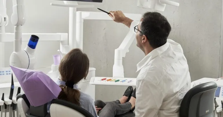 Dentista señala una pantalla mientras una paciente sentada en el sillón dental escucha la explicación