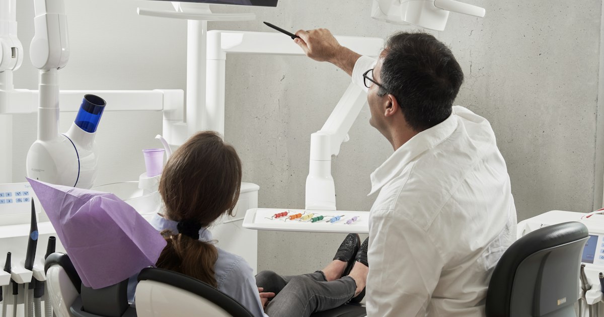 Dentista señala una pantalla mientras una paciente sentada en el sillón dental escucha la explicación