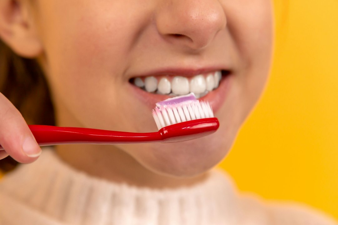 Mujer sonriente se cepilla los dientes con un cepillo rojo sobre fondo amarillo